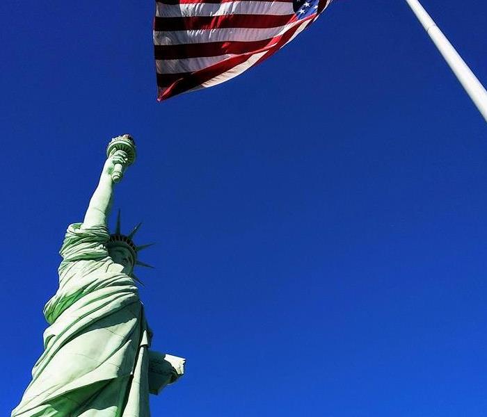 Statue of Liberty in front USA flag under blue sky Statue of Liberty in front USA flag under blue sky